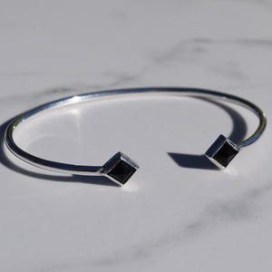 Silver bracelet with black square stones on a marble surface